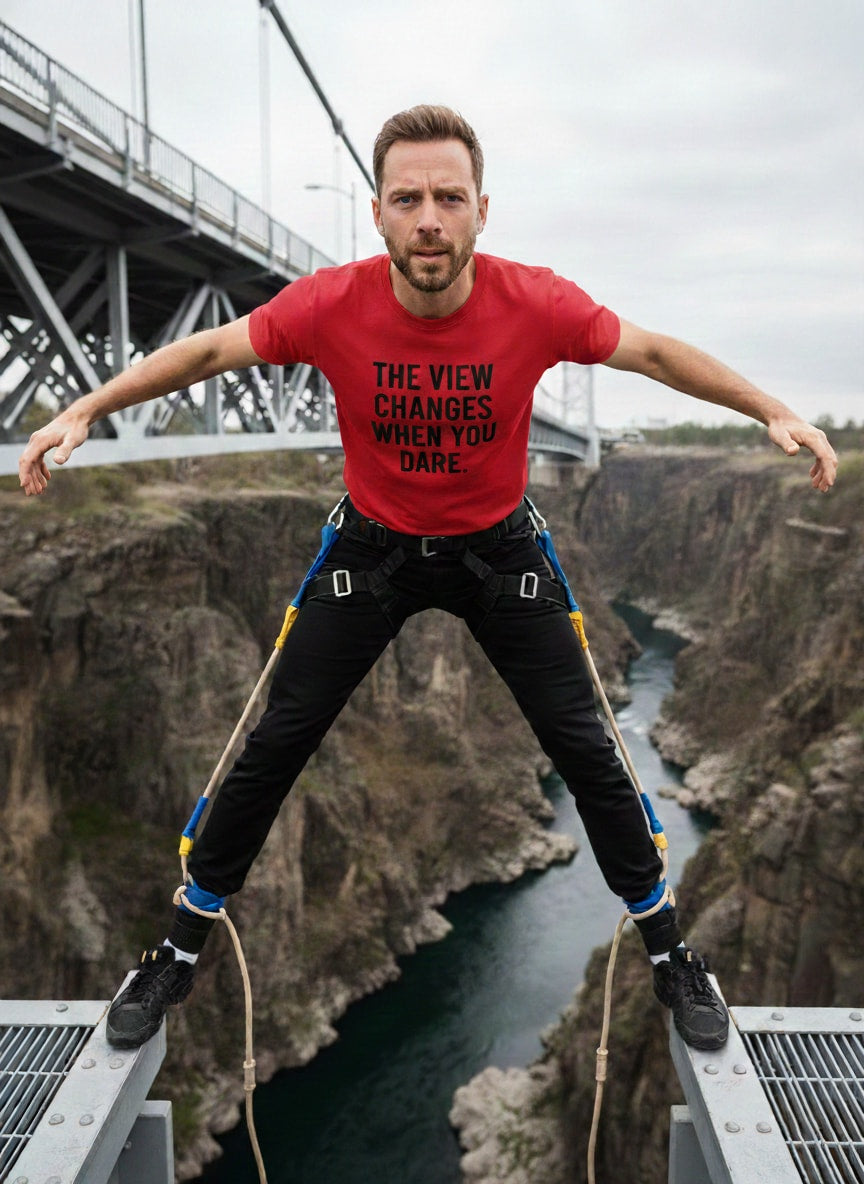 Risk and reward: man in THE VIEW CHANGES WHEN YOU DARE. red tee; great gift for an adventurer or a traveler who loves pushing boundaries