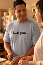 Cheerful man cooking dinner in the I L..e you shirt embracing a little mystery for his partner.