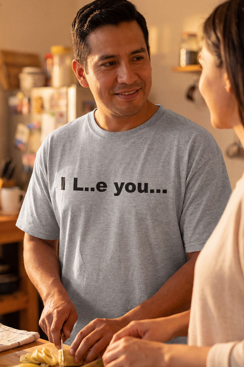Cheerful man cooking dinner in the I L..e you shirt embracing a little mystery for his partner.