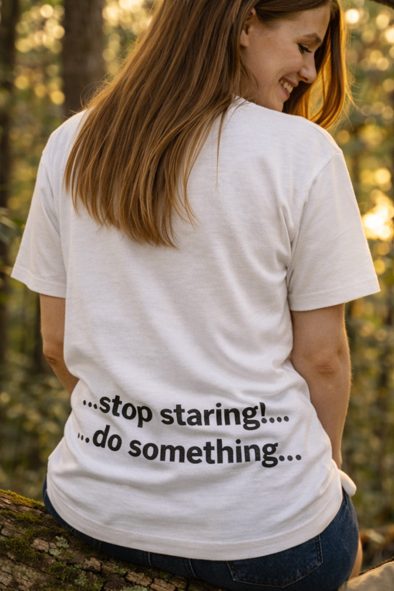 Smiling woman sitting outdoors wearing the stop staring do something shirt inviting bold actions from partners.