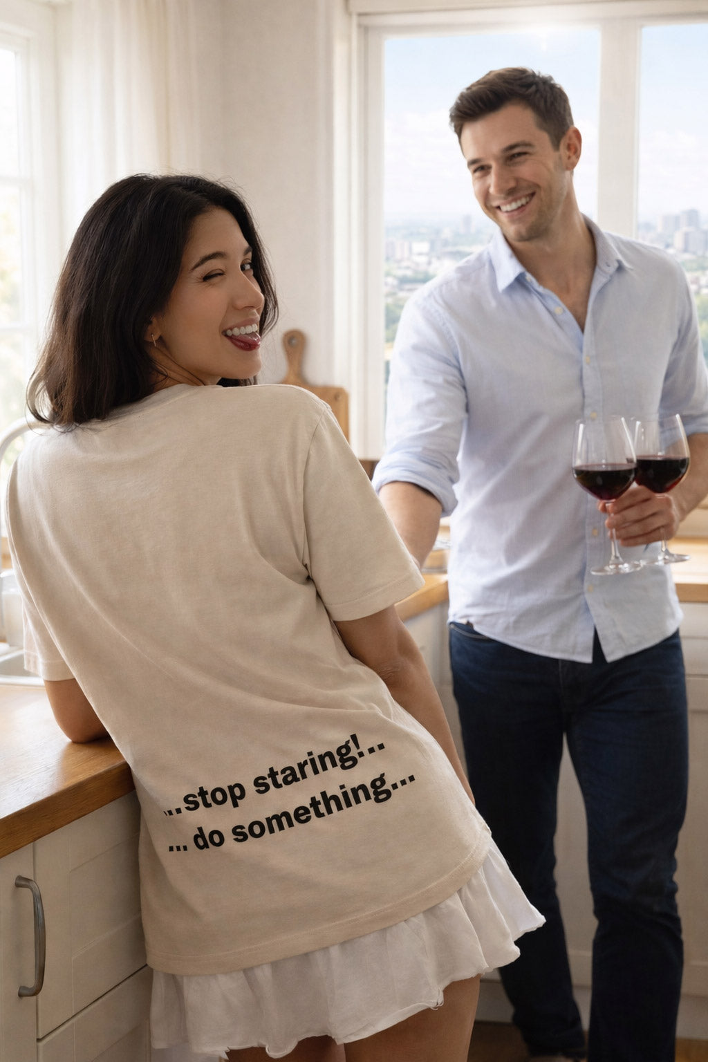 Happy woman holding wine in a kitchen wearing stop staring do something shirt for a spontaneous partner.