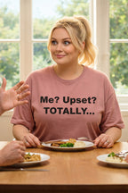 Smiling woman sitting at a dining table wearing the me upset totally tee expressing playfully passive-aggressive feelings.