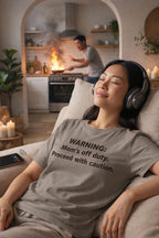 Calm woman wearing headphones in the warning mom's off duty proceed with caution shirt ignoring background chaos.
