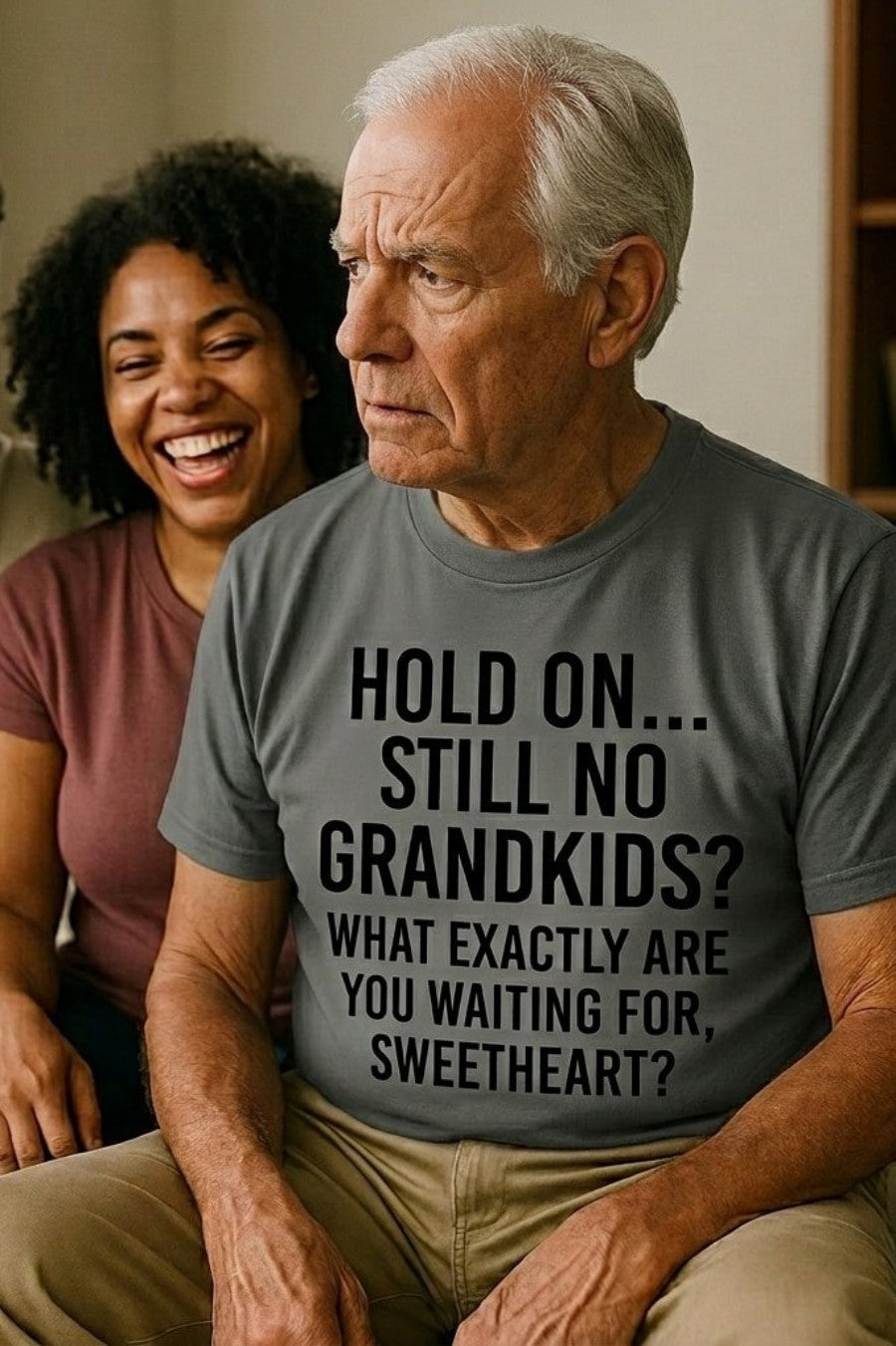 Older man sitting indoors wearing hold on still no grandkids disguising how deeply he cares, perfect gift.