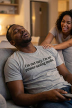 Tired man with remote wearing I'm not lazy I'm on power-saving mode enjoying peaceful stillness, ideal gift.